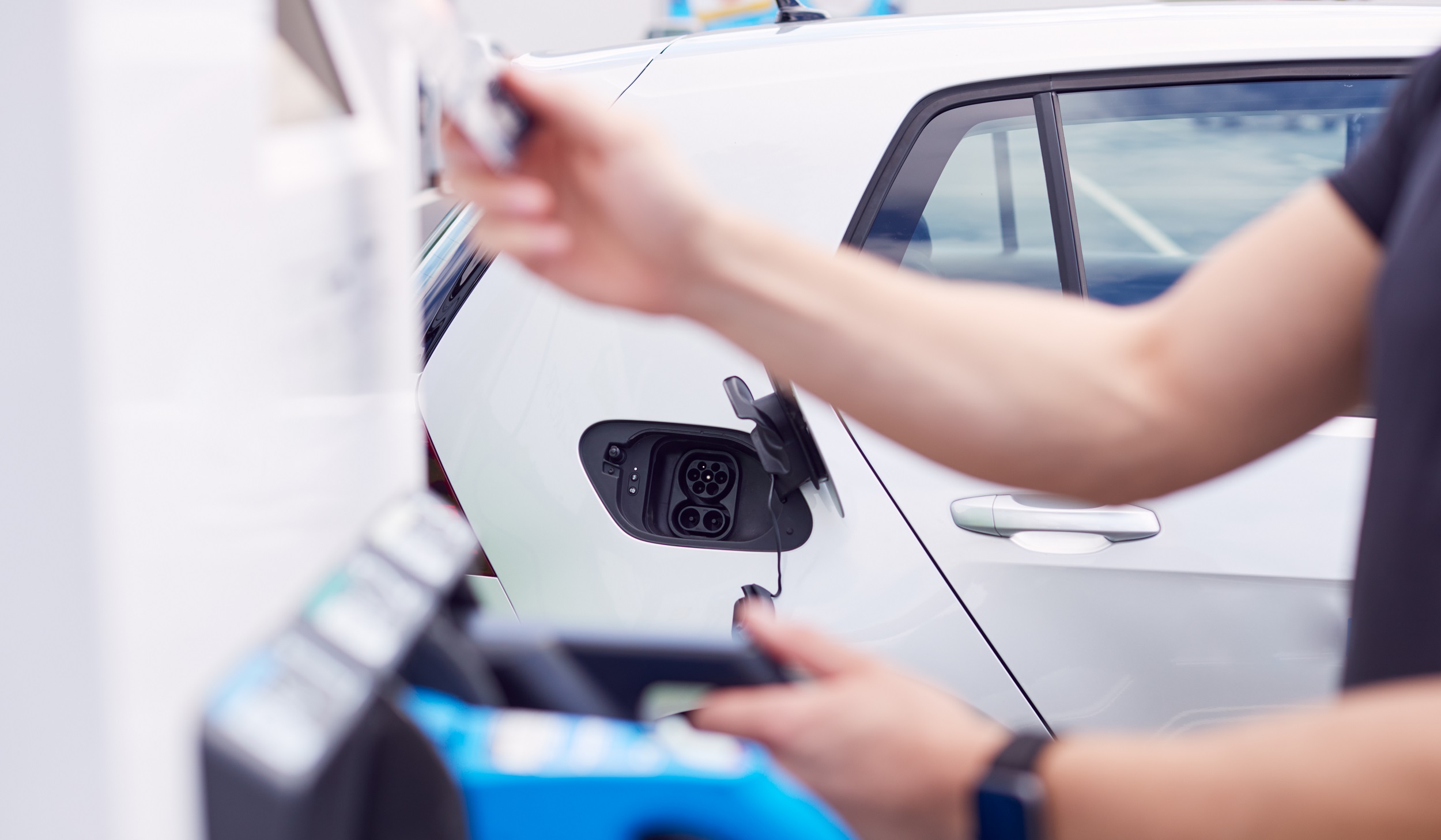 Man Charging Electric Vehicle Paying For Energy With Credit Card At Charging Station